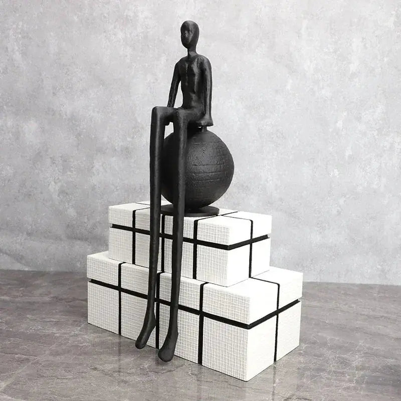 Modern matte black thinker sculpture with elongated limbs seated atop a textured matte black sphere