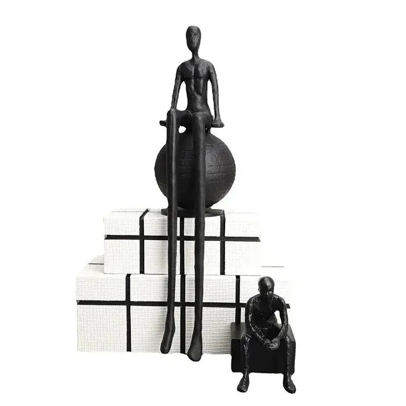 Modern matte black thinker sculpture featuring an abstract figurine with elongated limbs seated on a textured sphere