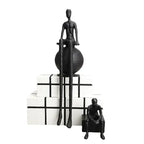 Modern matte black thinker sculpture featuring an abstract figurine with elongated limbs seated on a textured sphere