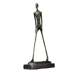 Abstract walking man sculpture in bronze with slender elongated figure and textured surface on a dark base