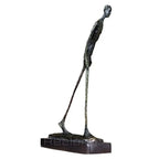 Abstract walking man sculpture bronze with textured surface slender elongated figure on dark rectangular base