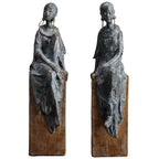 Two dark bronze african women sculpture figurines with long earrings and draped garments on wooden bases