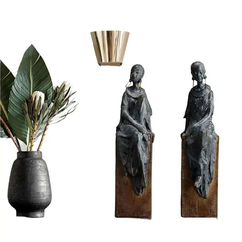 Dark gray textured ceramic vase holding green leaves and white flowers complementing african women sculpture decor