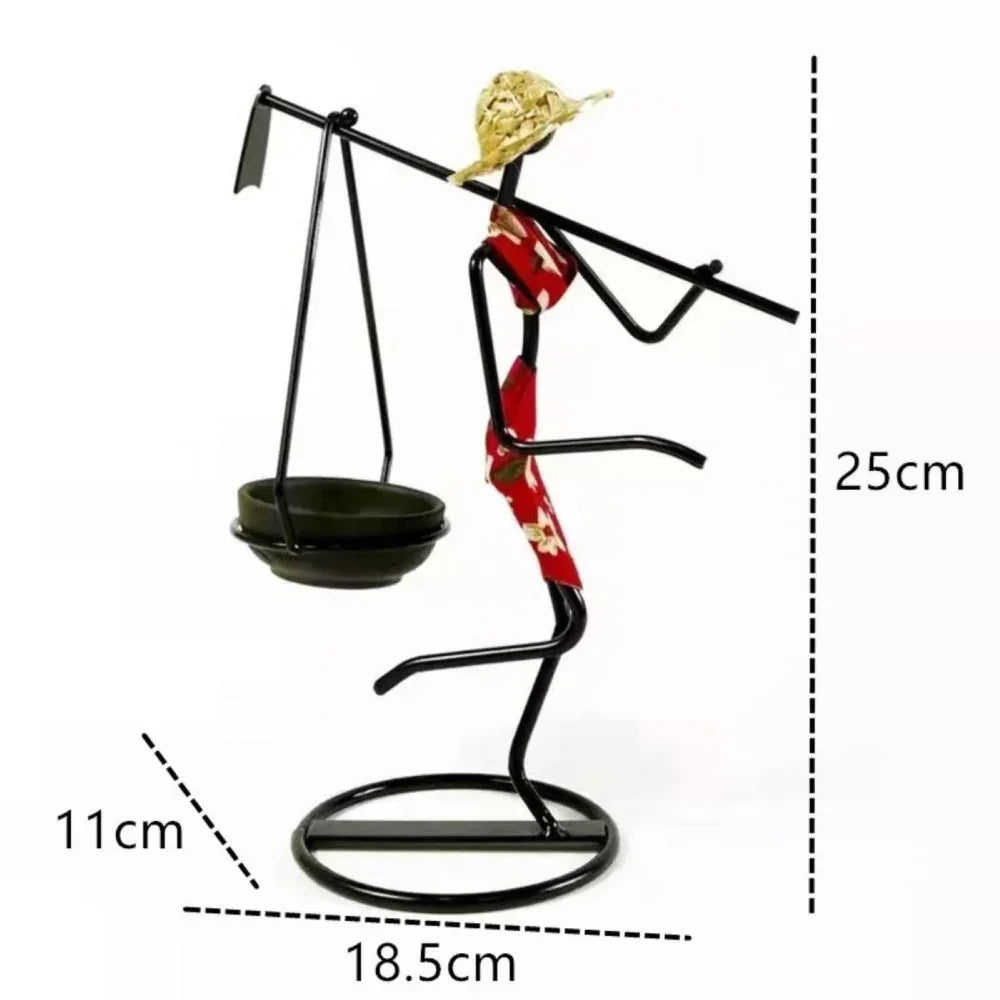 Black metal decorative candle holder shaped like a person in red patterned garment and gold hat holding balance scale