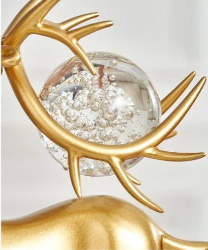 Golden deer figurine with crystal floral accents cradling a glass sphere filled with silver glitter and antlers